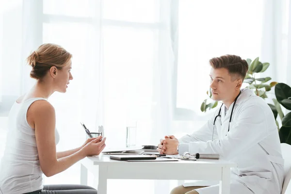 Handsome doctor in white coat looking at attractive patient in clinic — Stock Photo