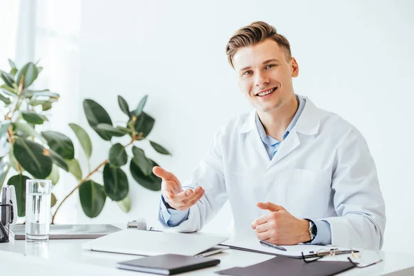 Guapo y alegre médico sonriendo mientras gesticulaba en la clínica - foto de stock