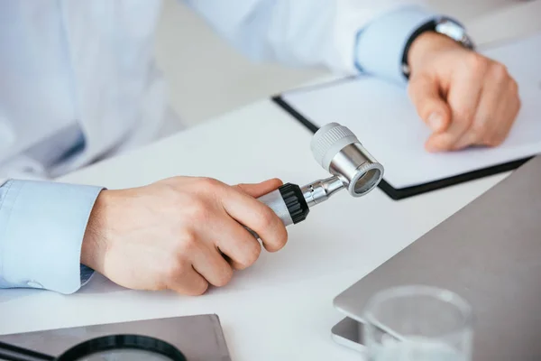 Vista recortada del dermatólogo que sostiene el dermatoscopio en la clínica - foto de stock