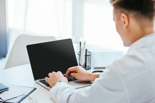 Enfoque selectivo del médico utilizando el ordenador portátil con pantalla en blanco - foto de stock