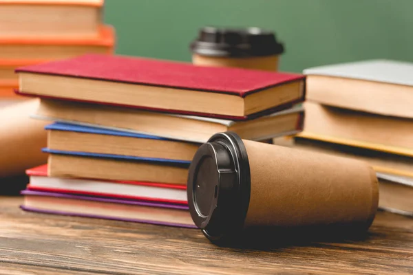 Books and disposable cups on wooden surface on green — Stock Photo