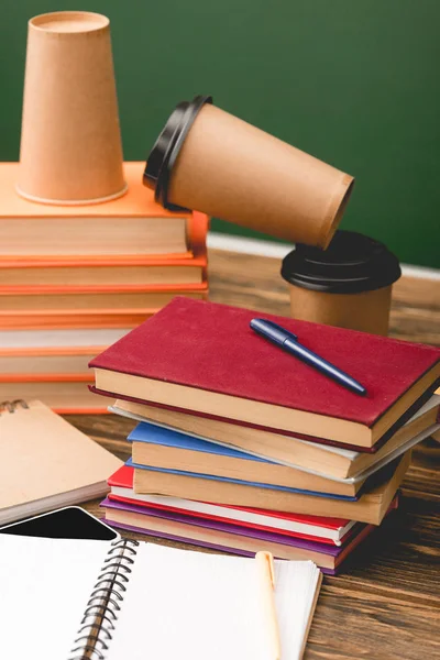 Messa a fuoco selettiva di libri, quaderni, penne, smartphone e tazze usa e getta su superficie in legno isolata su verde — Foto stock