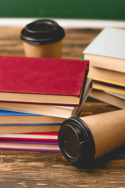 Foyer sélectif des livres et des tasses jetables sur la surface en bois sur vert — Photo de stock