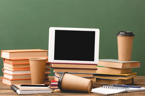 Books, notebooks, disposable cups, pens, smartphone and digital tablet with blank screen isolated on green — Stock Photo