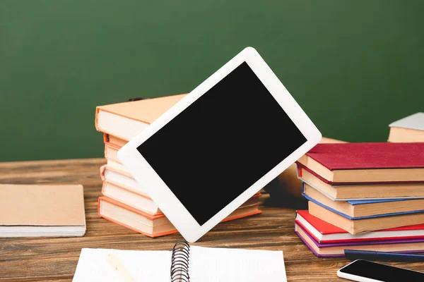 Libros, cuadernos, smartphone y tableta digital con pantalla en blanco sobre superficie de madera aislada en verde - foto de stock