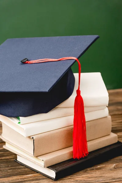 Books and academic cap on wooden surface isolated on green — Stock Photo