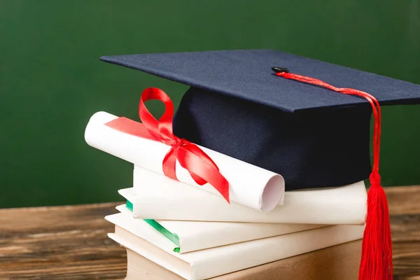 Libros, gorra académica y diploma sobre superficie de madera aislada en verde - foto de stock