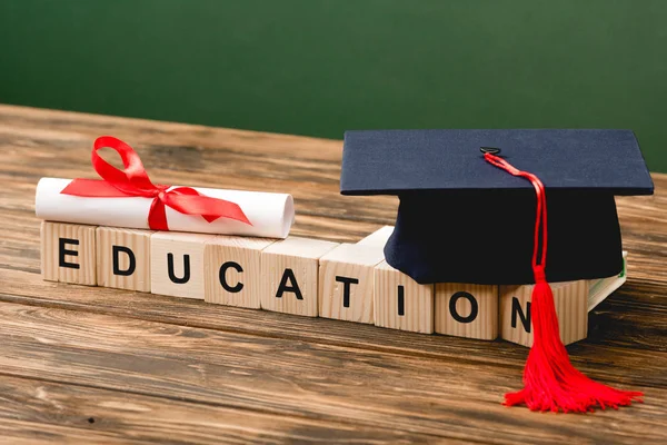 Wooden blocks with letters, academic cap and diploma on wooden surface isolated on green — Stock Photo