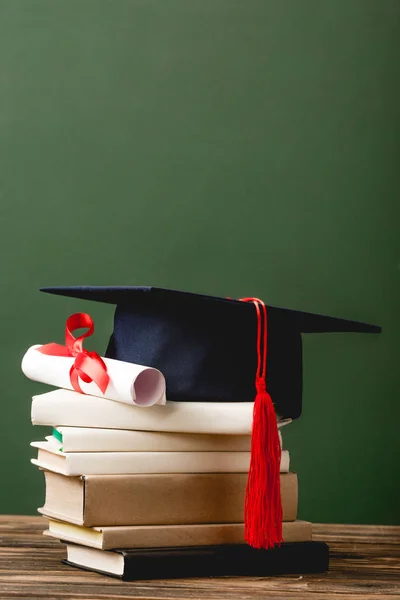 Livros, gorro acadêmico e diploma sobre superfície de madeira isolada em verde — Fotografia de Stock