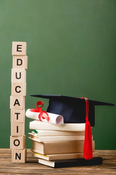 Blocchi di legno con lettere, libri, tappo accademico e diploma su superficie di legno isolata su verde — Foto stock