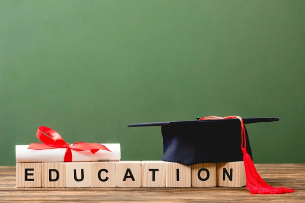 Blocs de bois avec lettres, diplôme et casquette académique sur surface en bois isolé sur vert — Photo de stock