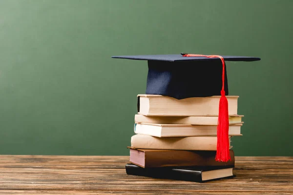 Livres et casquette académique sur surface en bois isolé sur vert — Photo de stock