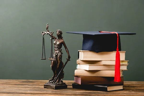 Bücherstapel, Themis-Statuette und akademische Mütze auf hölzerner Oberfläche auf grau — Stockfoto