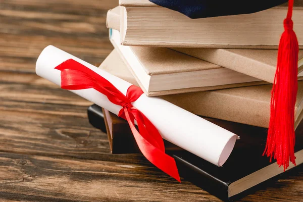 Diploma with ribbon and stack of books on wooden surface — Stock Photo