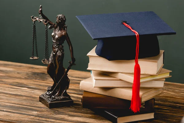 Themis estatuilla, pila de libros y la tapa académica en la superficie de madera en gris - foto de stock