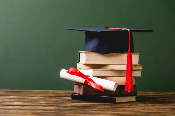 Books, academic cap and diploma on wooden surface isolated on green — Stock Photo