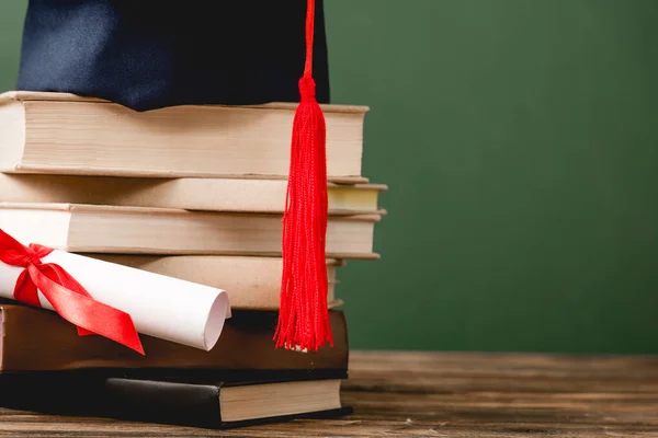 Libros, gorra académica y diploma sobre superficie de madera aislada en verde - foto de stock