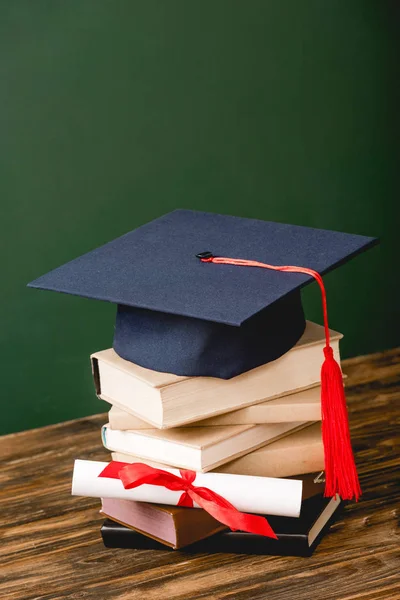 Books, academic cap and diploma on wooden surface on green — Stock Photo