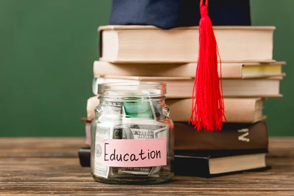 Libri, cappellino accademico e salvadanaio su superficie in legno isolata su verde — Foto stock