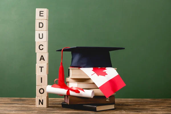 Holzblöcke mit Buchstaben, Diplom, Büchern, akademischer Mütze und kanadischer Flagge auf grüner Holzoberfläche — Stockfoto
