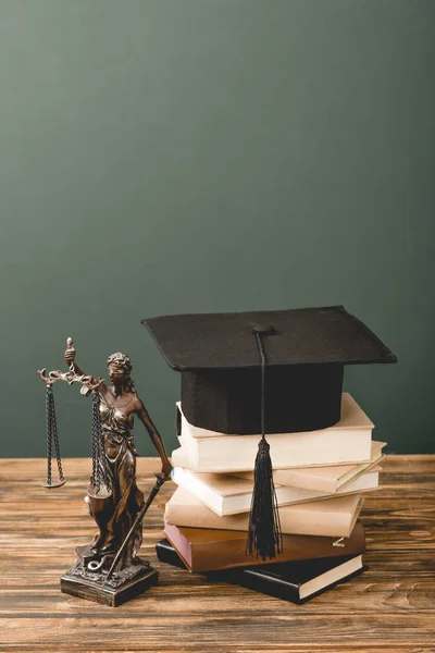 Themis estatuilla, libros y gorra académica sobre superficie de madera aislada en gris - foto de stock