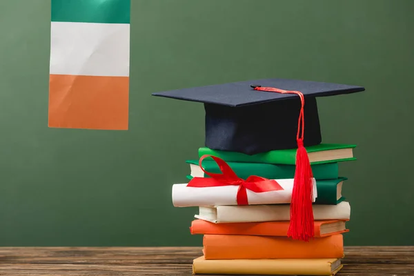 Книги, диплом, академическая шапка и ирландский флаг на деревянной поверхности изолированы на зеленый — стоковое фото