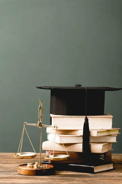 Books, academic cap and scales on wooden surface isolated on grey — Stock Photo