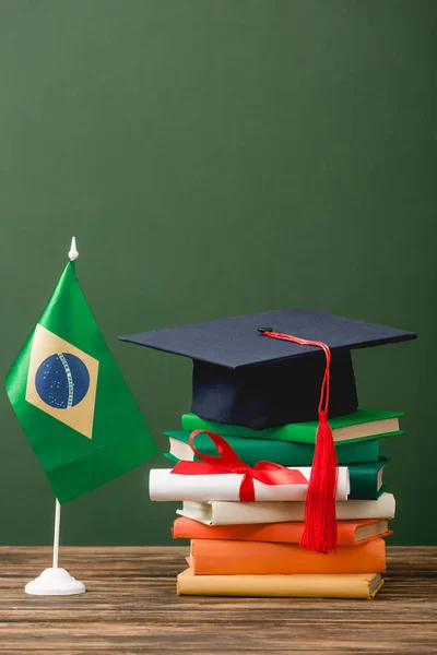 Bücher, Diplom, akademische Mütze und brasilianische Flagge auf hölzerner Oberfläche isoliert auf grün — Stockfoto