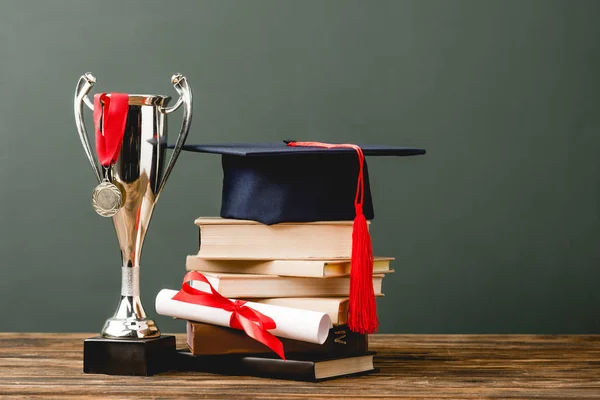 Books, diploma, academic cap, trophy cup and medal on wooden surface isolated on grey — Stock Photo