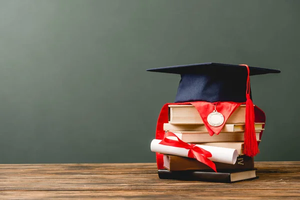 Books, academic cap, medal and diploma on wooden surface isolated on grey — Stock Photo