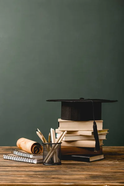 Books, academic cap, notebooks, scroll, pencils on wooden surface isolated on grey — Stock Photo