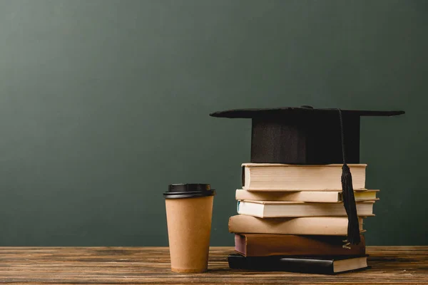 Livres, casquette académique et gobelet jetable sur surface en bois isolé sur gris — Photo de stock