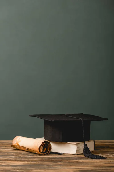 Libro, gorra académica y pergamino sobre superficie de madera aislado en gris - foto de stock