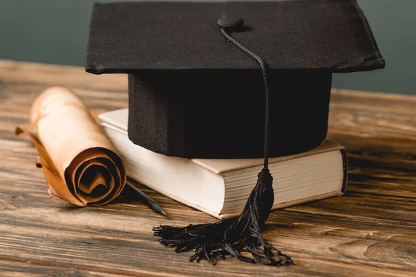 Book, academic cap and scroll on wooden surface isolated on grey — Stock Photo