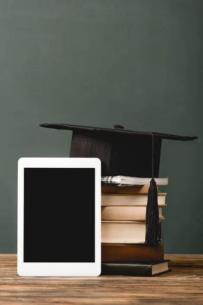Books, notebook, academic cap and digital tablet with blank screen on wooden surface isolated on grey — Stock Photo