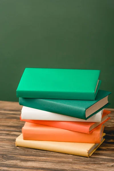 Stack of colorful books on wooden surface isolated on green — Stock Photo