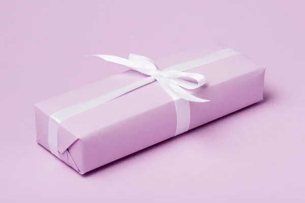 Gift box with white ribbon on purple surface — Stock Photo