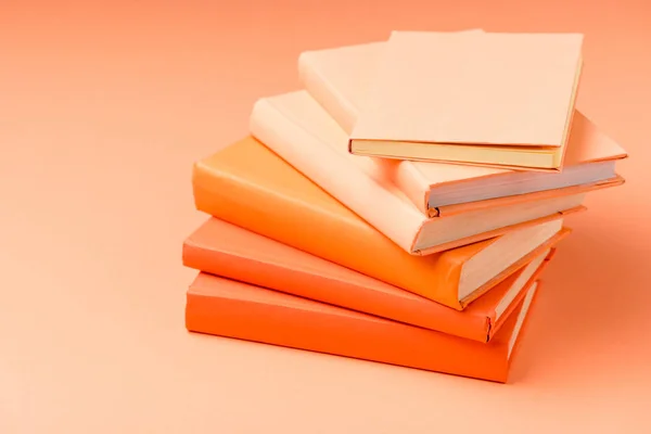 Pila de libros de tapa dura de colores en la superficie naranja - foto de stock