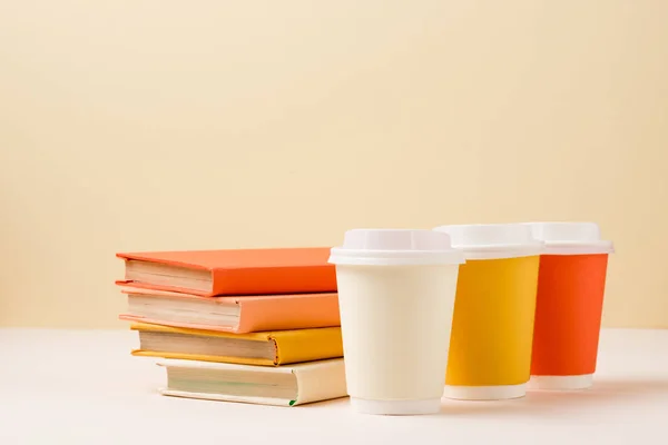 Pile de livres et gobelets jetables colorés sur surface blanche isolé sur beige — Photo de stock