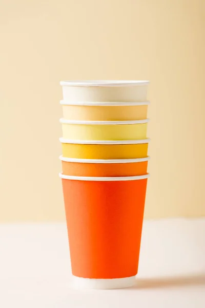 Tazas desechables de colores en la superficie blanca aislado en beige - foto de stock