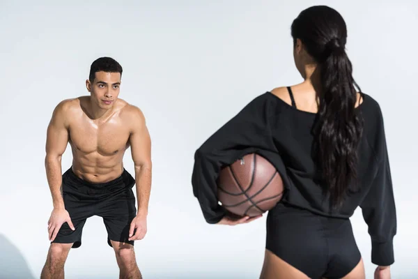 Handsome mixed race man looking at sportive african american woman with ball on white — Stock Photo