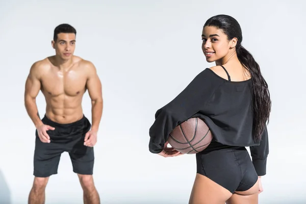 Selective focus of african american woman holding ball near mixed race man in black shorts on white — Stock Photo