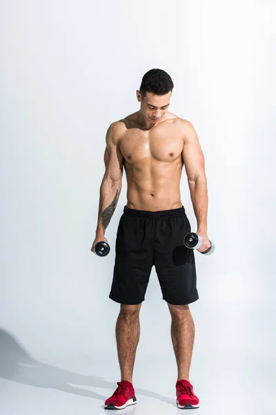 Handsome mixed race man holding dumbbells and looking down on white — Stock Photo