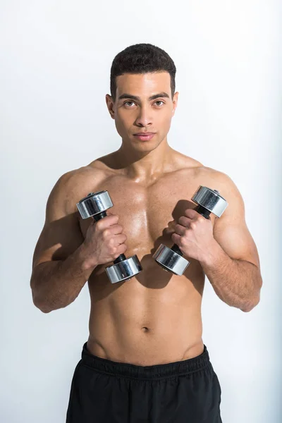 Athletic mixed race man holding dumbbells and looking at camera on white — Stock Photo