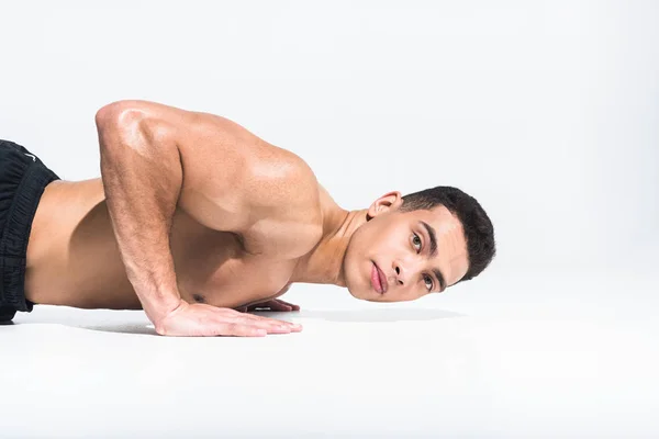 Bonito esportivo misto raça homem fazendo push ups e olhando para câmera no branco — Fotografia de Stock