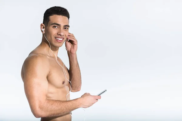 Handsome athletic mixed race man listening music in earphones and looking at camera on white — Stock Photo