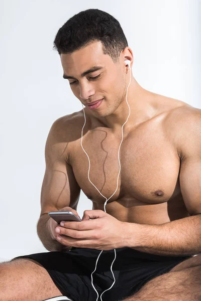 Handsome athletic man with smartphone listening music and smiling on white — Stock Photo