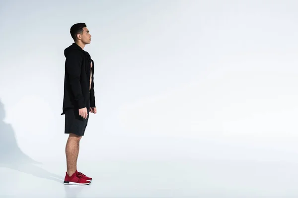 Side view of sportive mixed race man in black sportswear and red sneakers on white background with copy space — Stock Photo