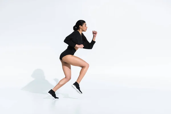 Side view of beautiful sportive african american girl in black sportswear running on white — Stock Photo