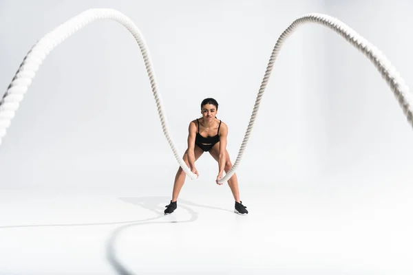 Enfoque selectivo de la chica afroamericana deportiva haciendo ejercicio con cuerdas en blanco - foto de stock